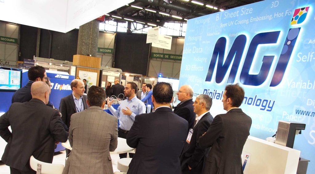 photo of MGI Digital Technology's booth at a trade show with visitors listening to an employee speak